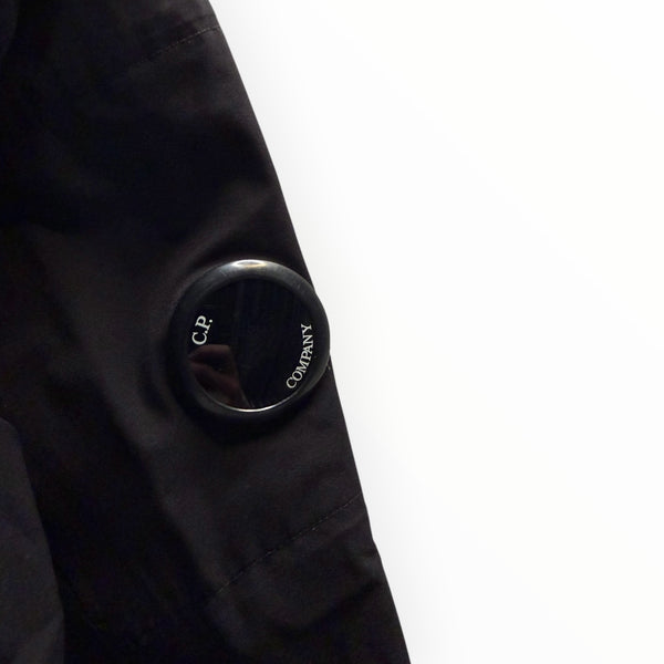 Détail de la lentille emblématique noire sur la manche d'une veste technique Secondstore C.P. Company en tissu Pro-Tek