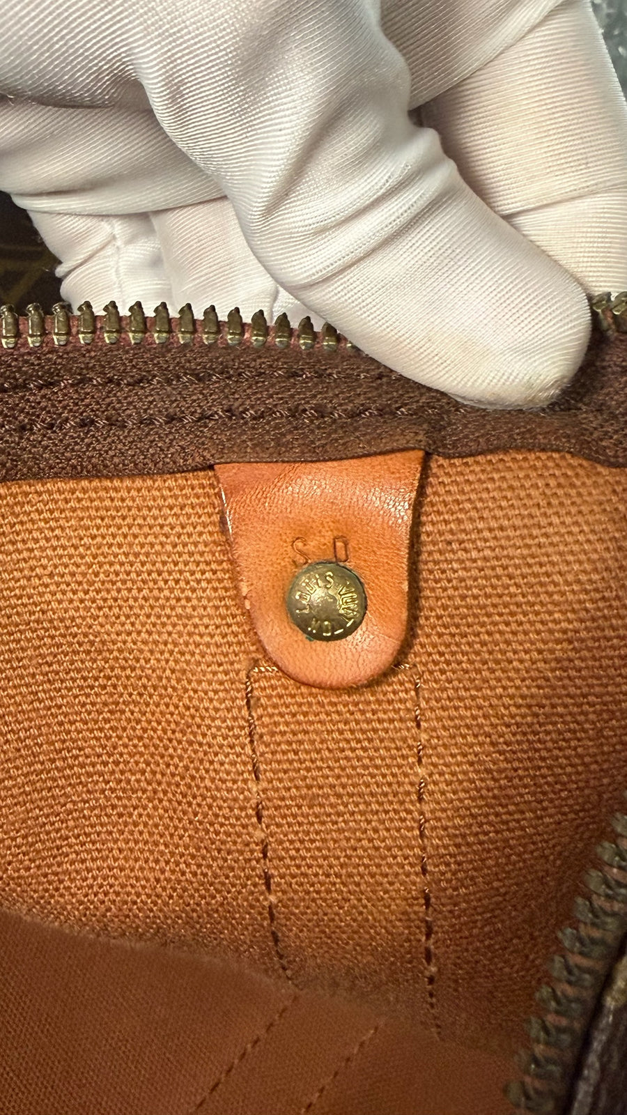 Gros plan sur le bouton pression en laiton doré gravé Louis Vuitton à l'intérieur du sac Secondstore Keepall