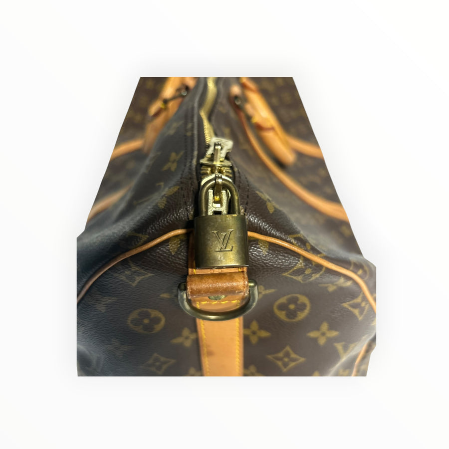 Détail du cadenas doré sur le sac de voyage Secondstore Louis Vuitton Keepall en toile Monogram et cuir naturel