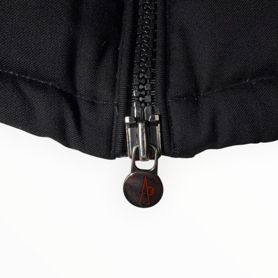 Gros plan sur la fermeture éclair noire d'une doudoune Secondstore Moncler avec tirette métallique siglée