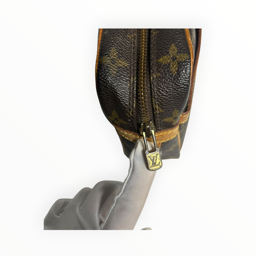 Gros plan sur la fermeture éclair dorée et le logo Secondstore d'une pochette Louis Vuitton en toile Monogram