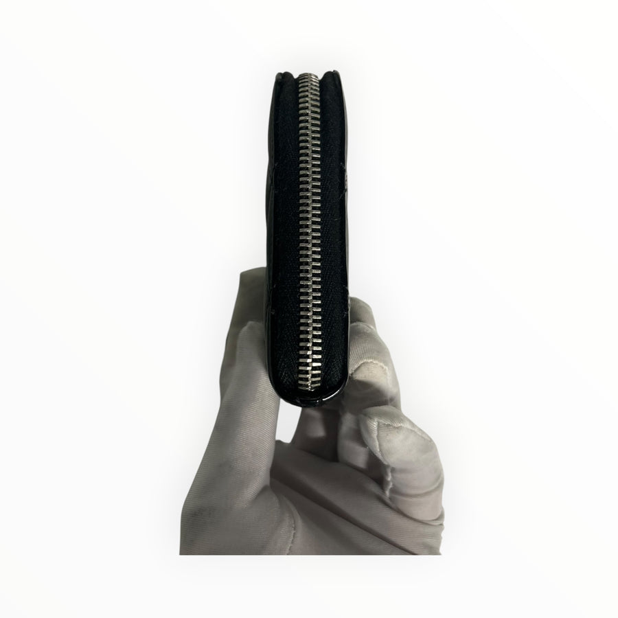 Portefeuille Secondstore Chanel matelassé en cuir verni noir avec fermeture éclair argentée vue de profil