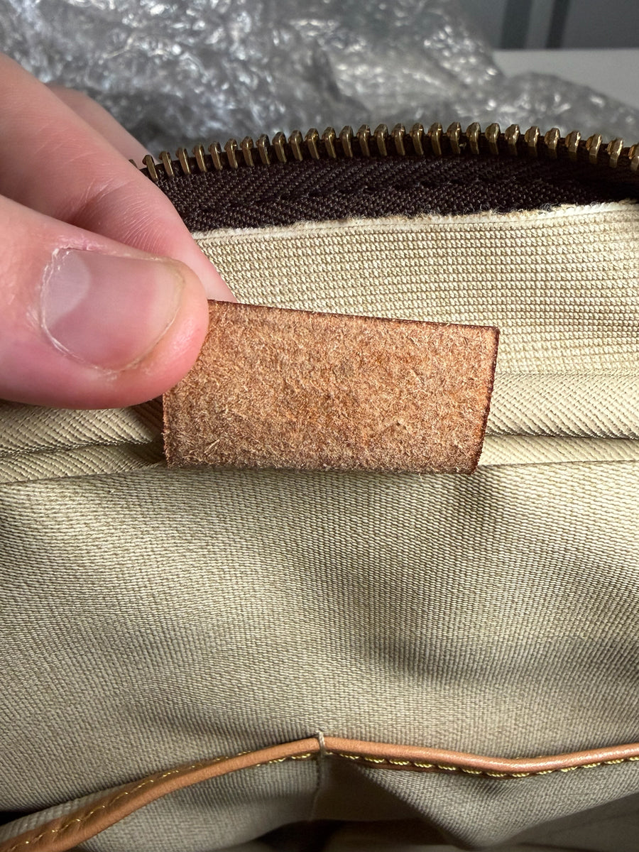 Détail de l'étiquette intérieure en cuir brut d'un sac de voyage Secondstore Louis Vuitton avec doublure textile beige