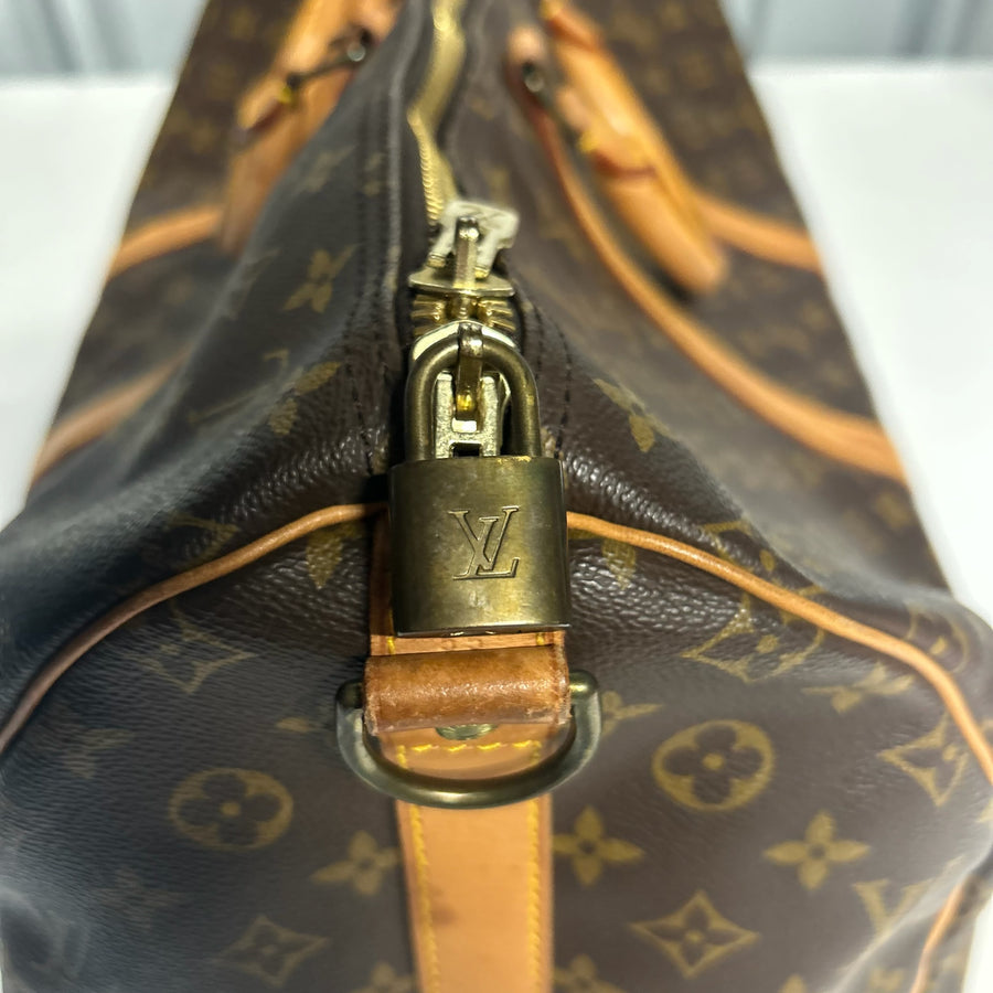 Détail du cadenas doré et fermeture éclair sur un sac de voyage Secondstore Louis Vuitton Keepall en toile Monogram