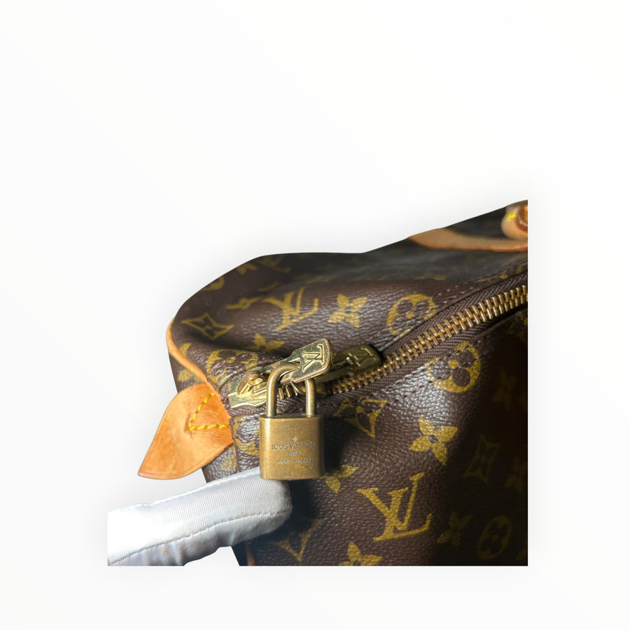 Détail du cadenas en laiton doré sur un sac de voyage Secondstore Louis Vuitton Keepall en toile Monogram marron