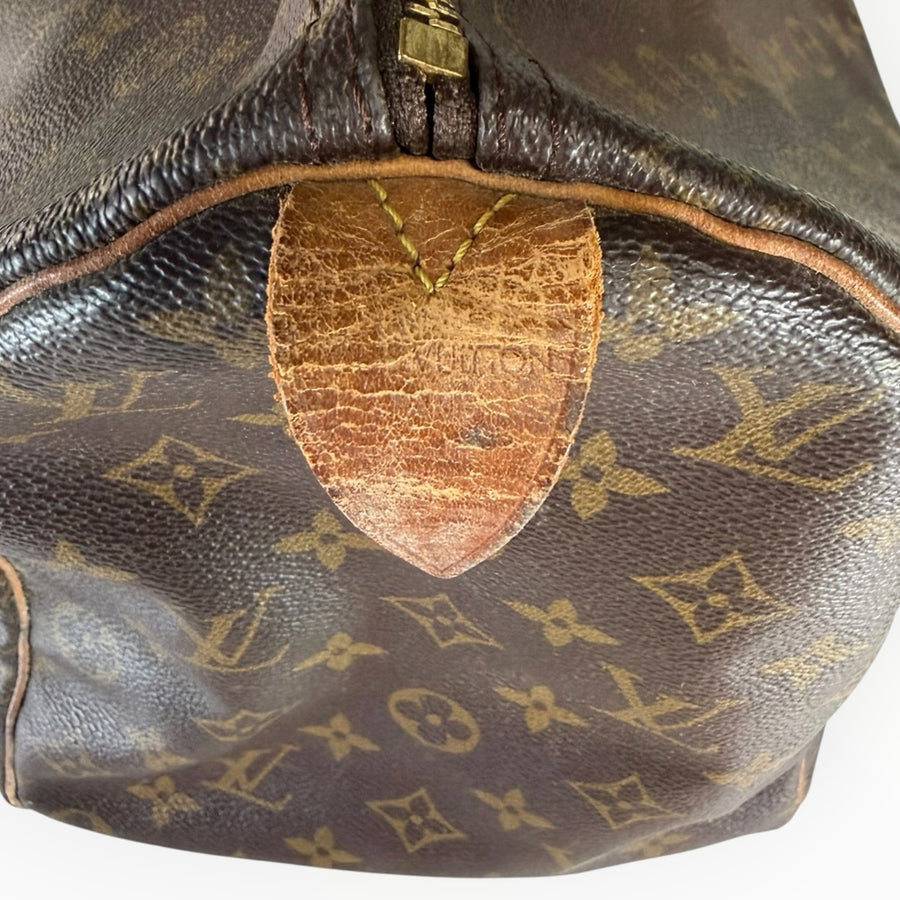 Détail de la patine sur la languette en cuir d'un sac de voyage Secondstore Louis Vuitton Speedy en toile Monogram