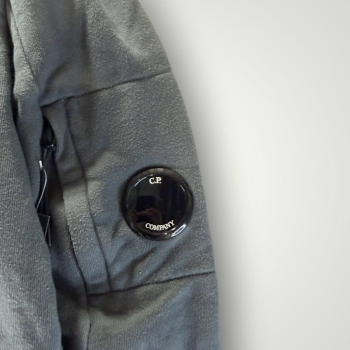 Détail de la manche d'un sweat-shirt gris Secondstore C.P. COMPANY avec poche zippée et lentille iconique noire