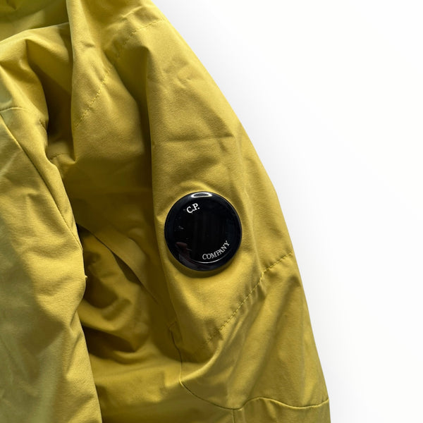 Détail de la manche d'une veste jaune Secondstore C.P. Company en tissu technique avec la lentille emblématique