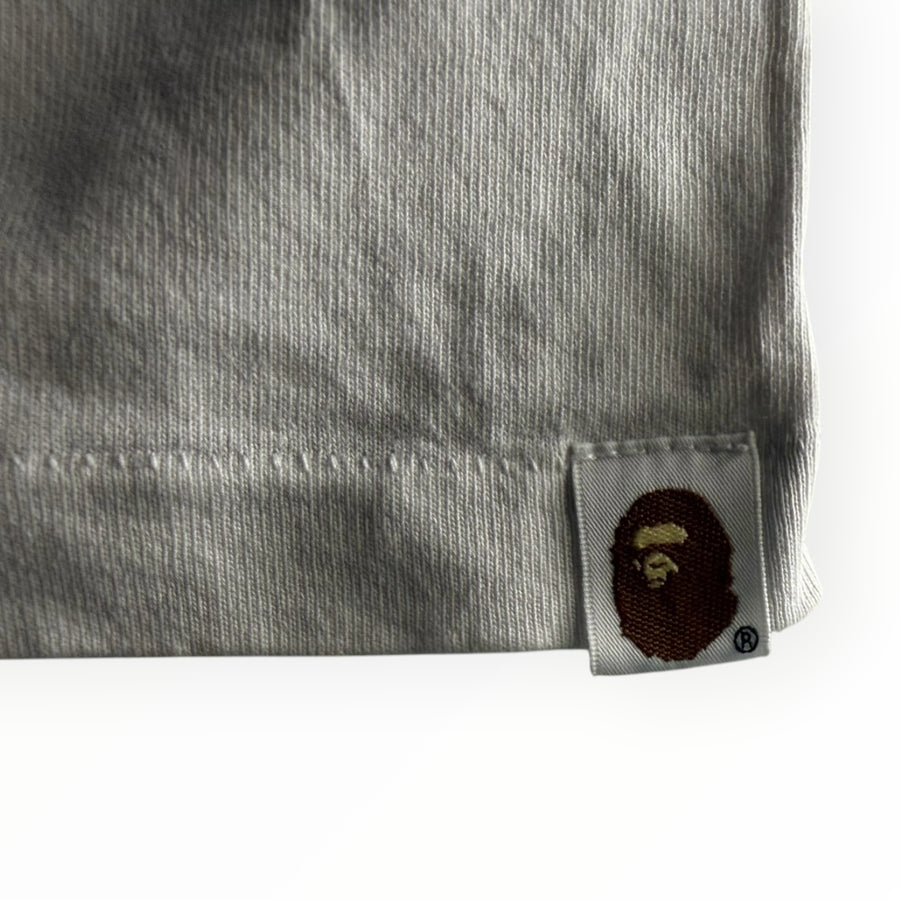 Gros plan sur l'étiquette tissée Ape Head sur la manche d'un t-shirt Secondstore A BATHING APE en coton gris