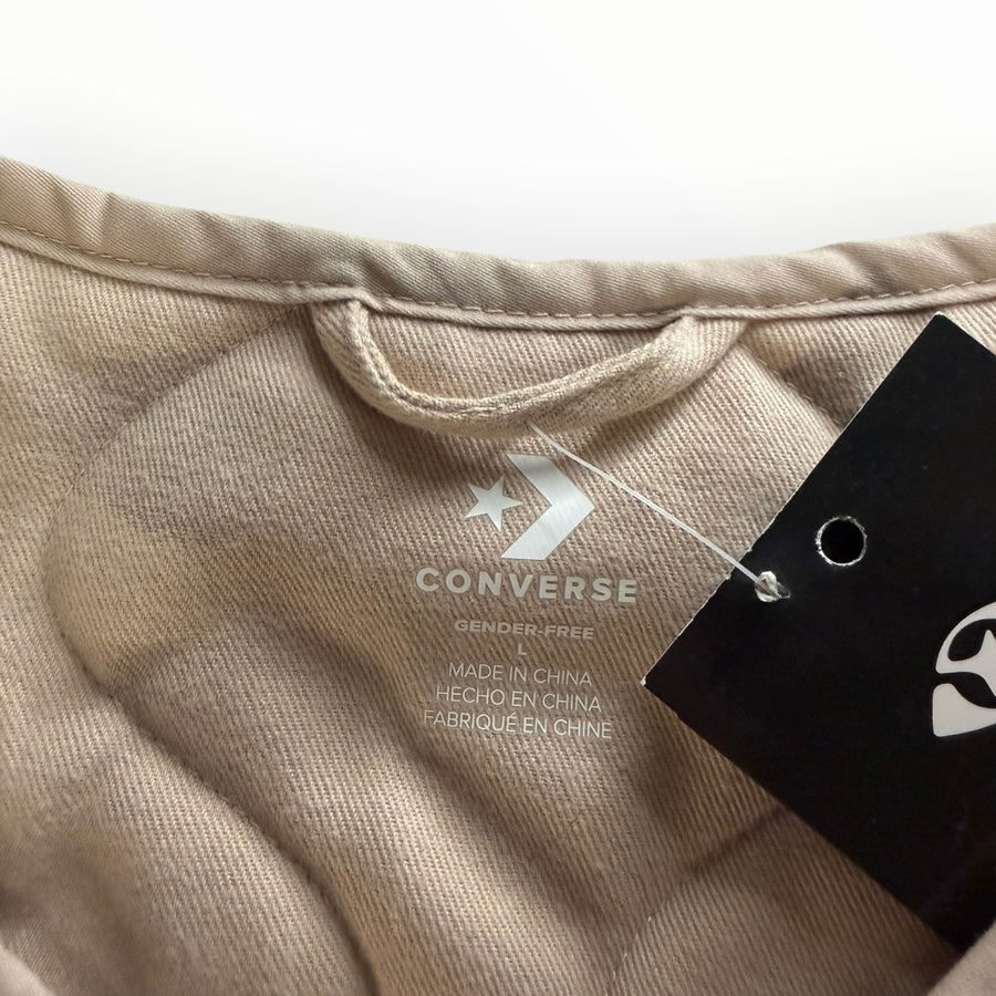 Gros plan sur l'étiquette intérieure d'une veste matelassée beige Secondstore Converse avec logo et taille L