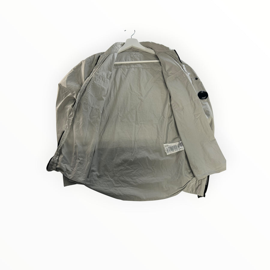 Secondstore light grey C.P. Company zip-up overshirt with iconic sleeve lens detail, shown open on a hanger.