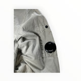 Secondstore light grey C.P. Company overshirt sleeve featuring the iconic black lens detail on a utility pocket.