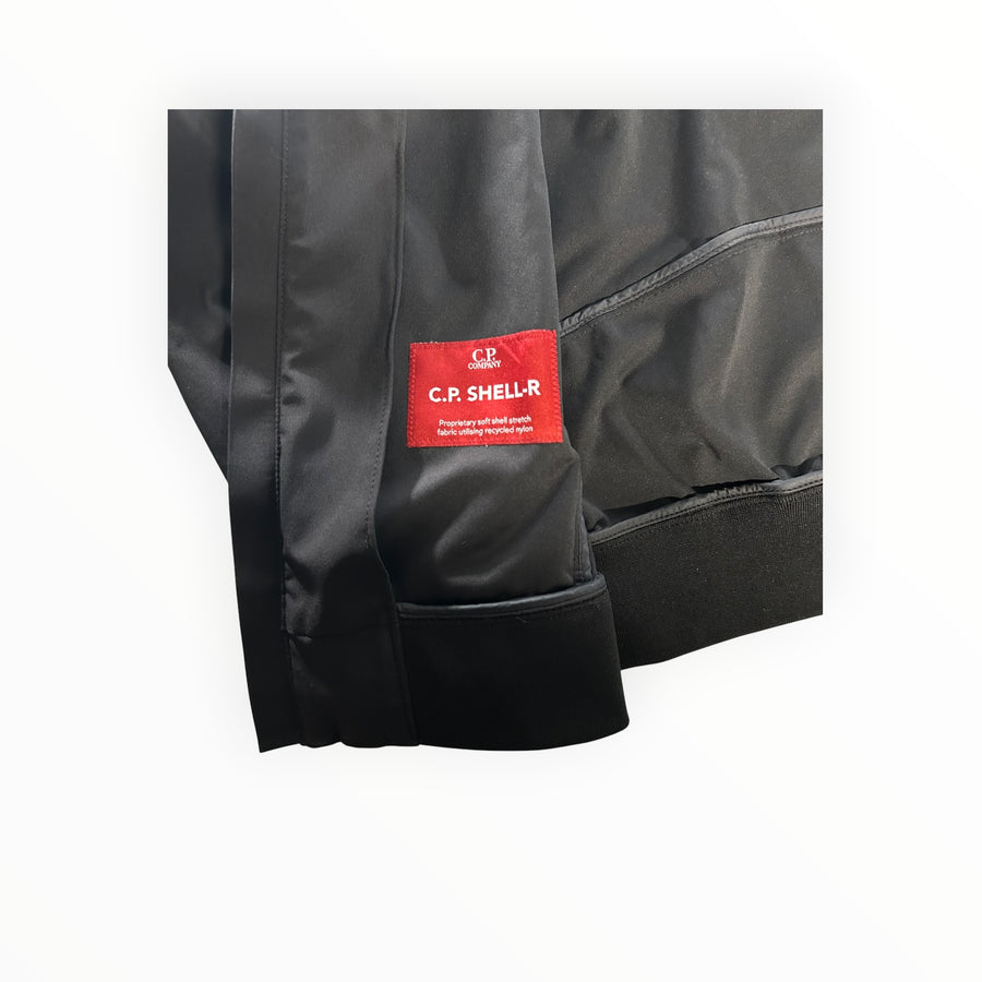 Détail de l'étiquette rouge C.P. Company Shell-R sur une veste noire en nylon recyclé Secondstore