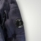 Détail de la manche d'un sweat-shirt Secondstore C.P. Company bleu marine avec sa poche zippée et sa lentille iconique