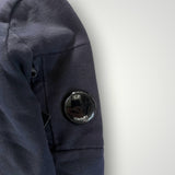 Détail de la manche d'un sweat-shirt Secondstore C.P. COMPANY bleu marine avec poche zippée et lentille iconique