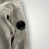 Détail de la manche beige du sweat-shirt Secondstore C.P. Company avec sa lentille emblématique sur poche zippée