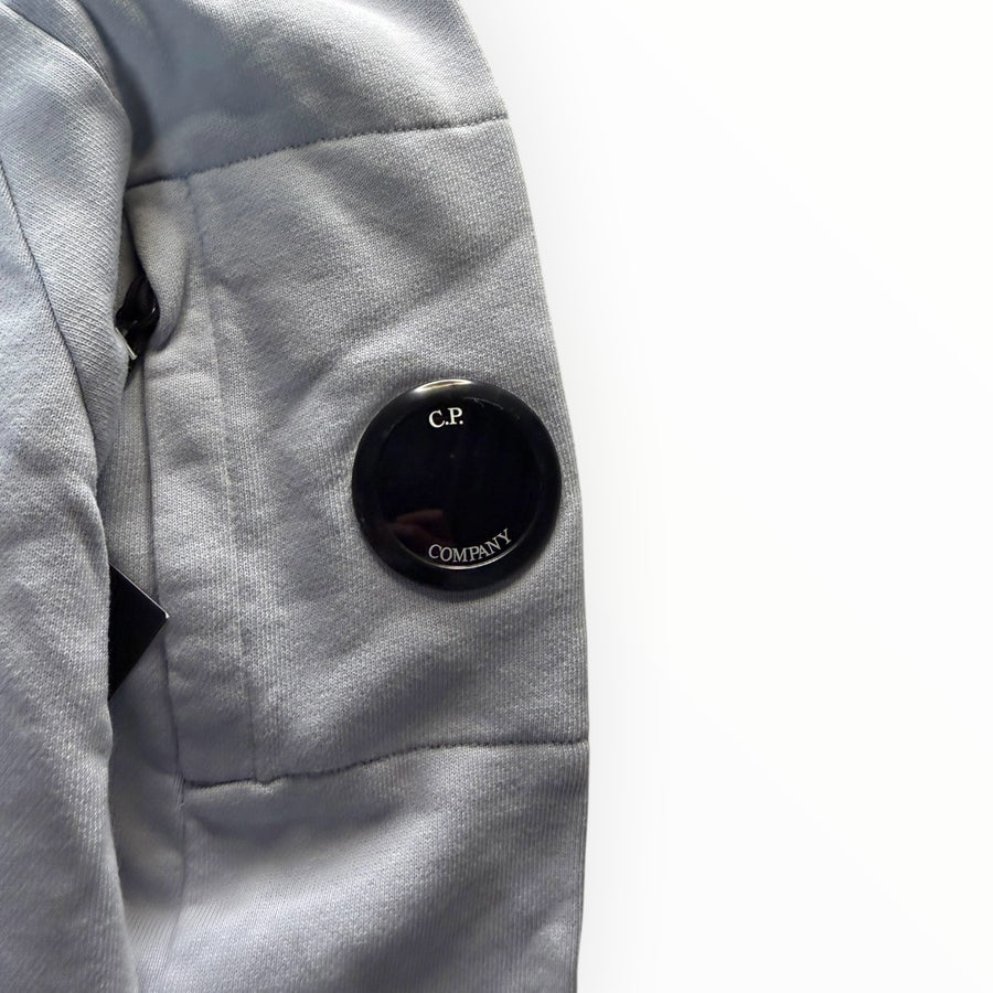 Détail de la manche d'un sweat-shirt Secondstore C.P. Company bleu ciel avec la lentille iconique noire