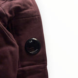Détail de la manche bordeaux du sweat-shirt Secondstore C.P. Company avec sa lentille emblématique noire
