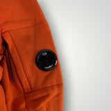 Détail de la manche orange d'un sweat-shirt Secondstore C.P. Company avec la lentille signature sur poche zippée