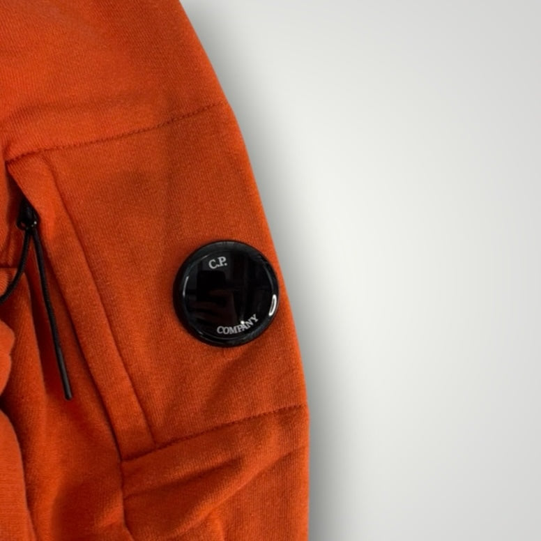 Détail de la manche orange d'un sweat-shirt Secondstore C.P. Company avec la lentille signature sur poche zippée