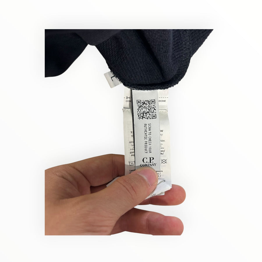 Secondstore C.P. Company sweatshirt interior care label with authentication QR code held by a hand