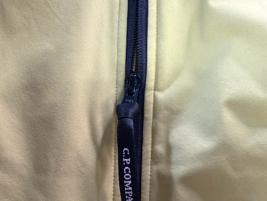 Gros plan sur la fermeture éclair bleu marine avec logo Secondstore C.P. Company sur une veste technique jaune