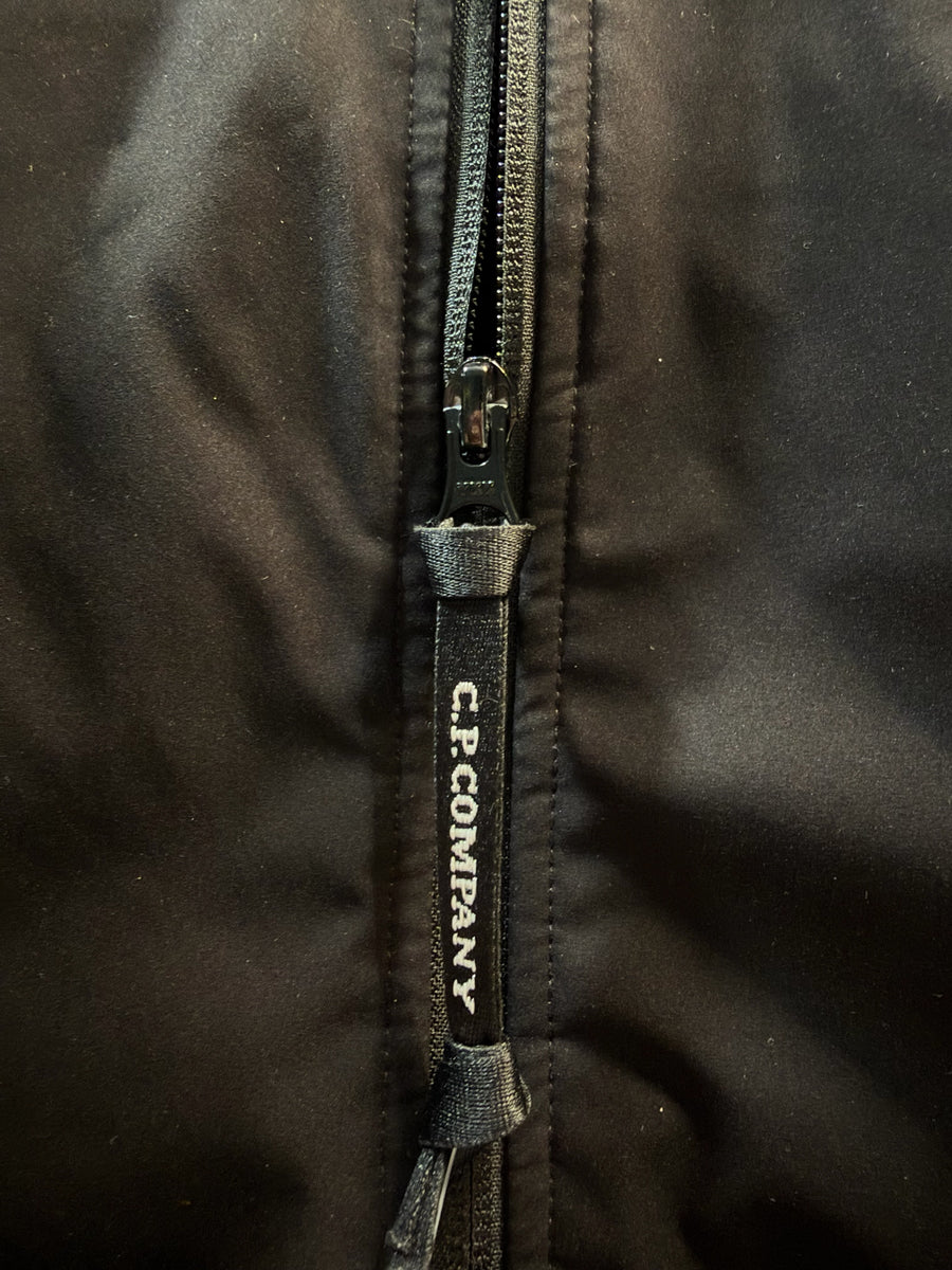 Gros plan sur la tirette de fermeture éclair noire avec logo Secondstore C.P. Company sur une veste technique