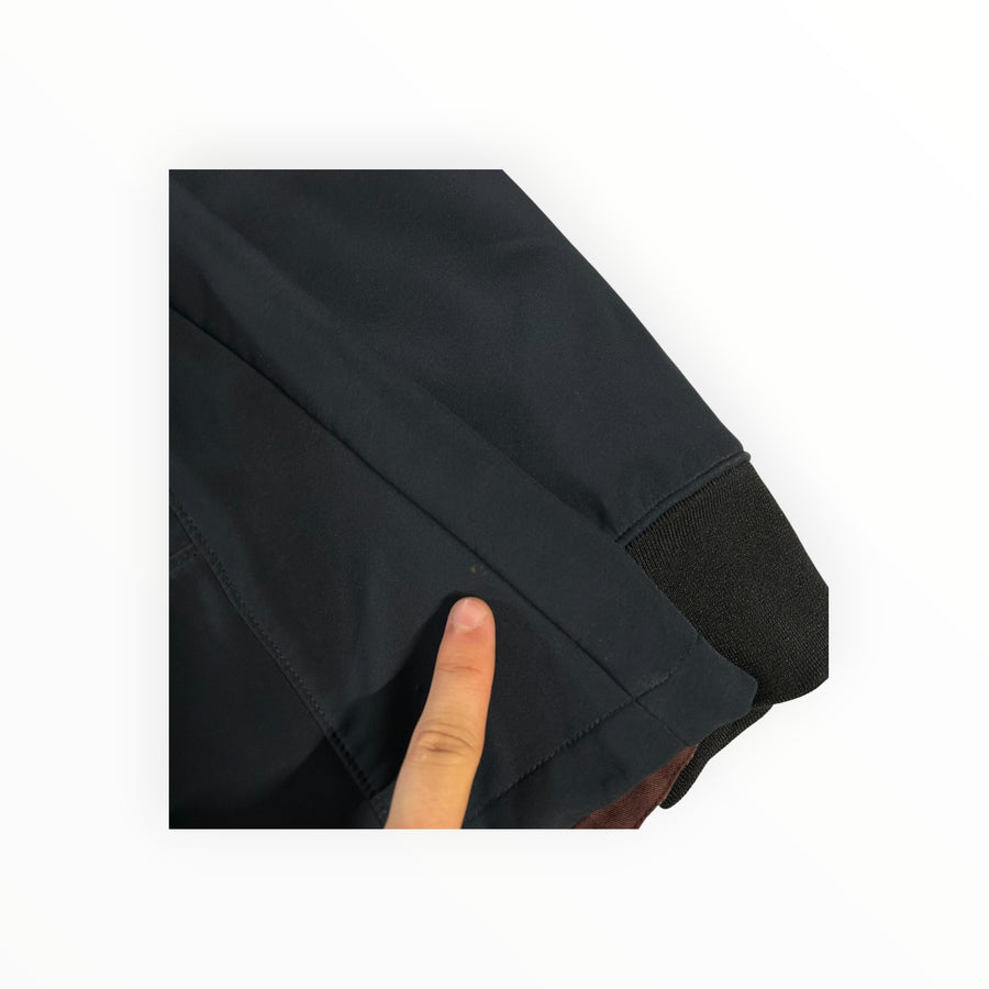 Détail de la veste noire C.P. Company Goggle en tissu soft shell avec poignet côtelé et doublure bordeaux.