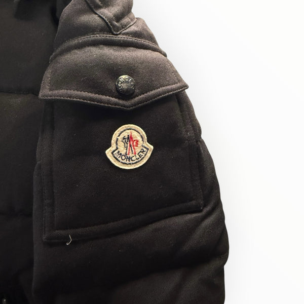Détail de la manche d'une doudoune noire Secondstore Moncler avec écusson logo emblématique et poche à rabat