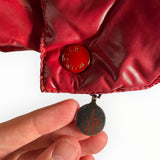 Gros plan sur le bouton-pression gravé et la tirette de fermeture éclair du gilet sans manches rouge Secondstore Moncler