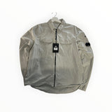 Secondstore light grey C.P. Company zip-up overshirt with chest pockets and iconic sleeve lens detail on a hanger.