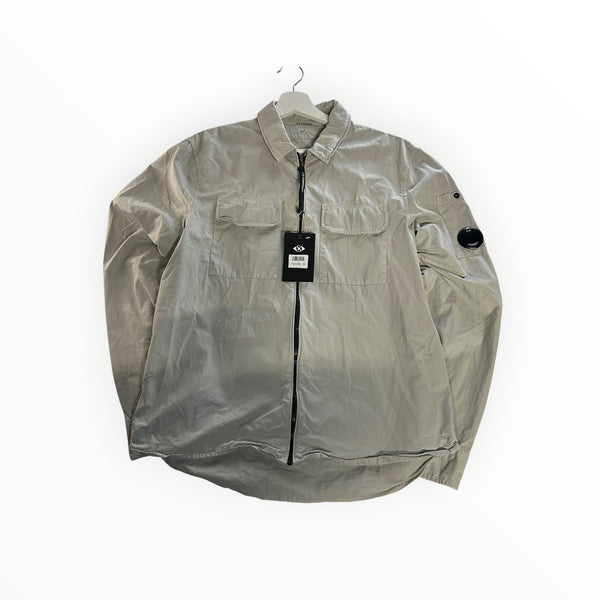 Secondstore light grey C.P. Company zip-up overshirt with chest pockets and iconic sleeve lens detail on a hanger.