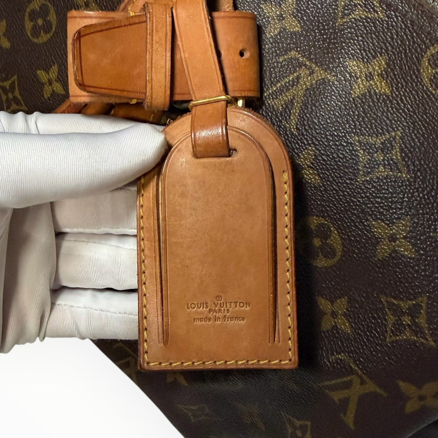 Porte-adresse en cuir naturel Secondstore sur un sac de voyage Louis Vuitton Keepall en toile Monogram emblématique
