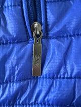 Gros plan sur la tirette de fermeture éclair métallique marquée PJS d'un gilet Secondstore Parajumpers bleu matelassé