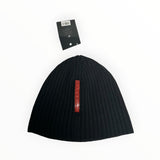 Secondstore black ribbed knit Prada beanie with a vertical red logo plaque and attached brand tag.