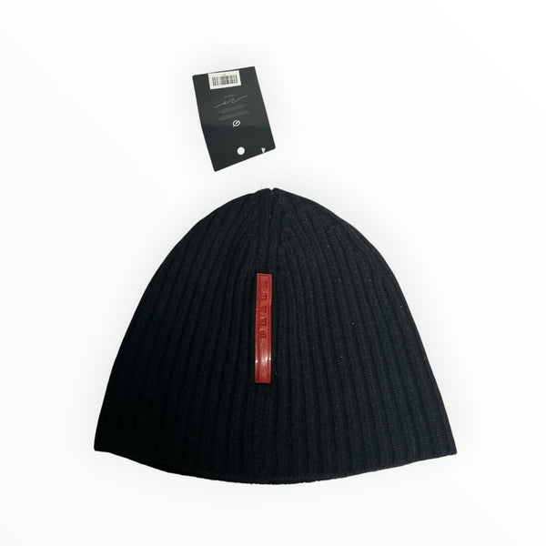 Secondstore black ribbed knit Prada beanie with a vertical red logo plaque and attached brand tag.