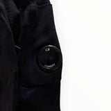 Détail de la lentille iconique noire sur la manche d'un pull en coton Secondstore C.P. Company