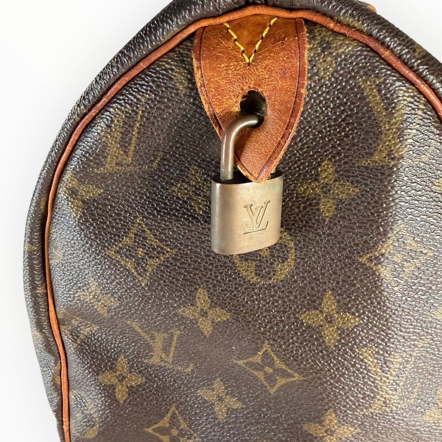 Gros plan sur le cadenas en laiton doré d'un sac Secondstore Louis Vuitton Speedy en toile Monogram et cuir patiné