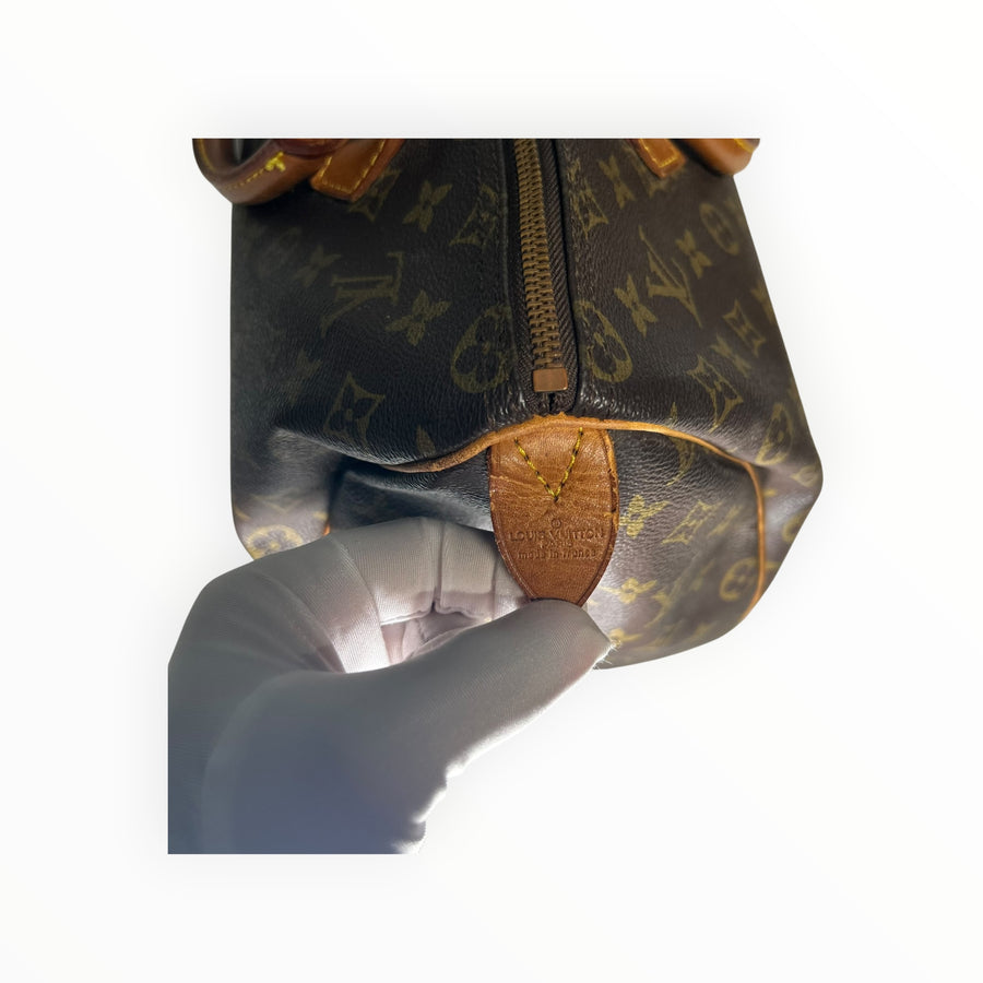 Détail de la patte en cuir avec marquage Louis Vuitton sur un sac Speedy en toile Monogram chez Secondstore