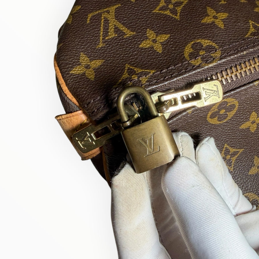 Détail du cadenas doré et fermeture éclair sur le sac de voyage Secondstore Louis Vuitton Keepall en toile Monogram