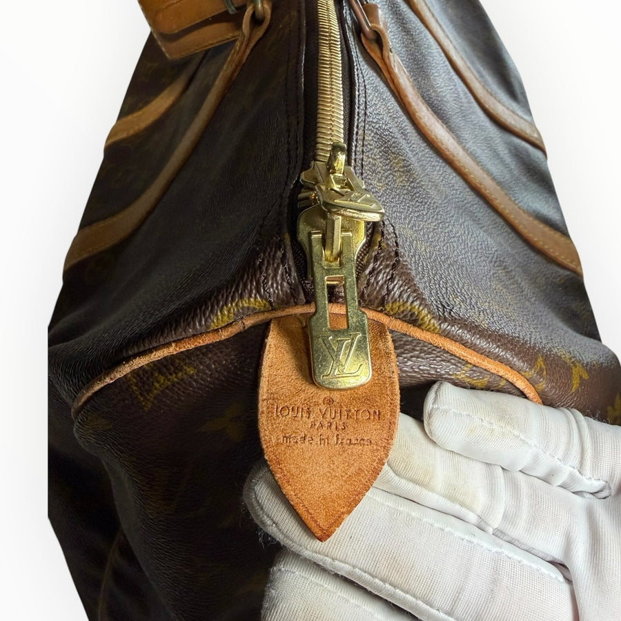 Gros plan sur la fermeture éclair dorée et l'étiquette en cuir du sac de voyage Secondstore Louis Vuitton Keepall