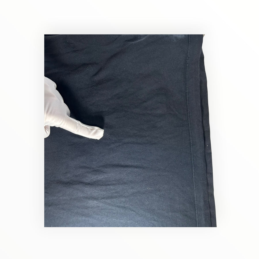 Gloved hand pointing to a small snag on a black cotton Stone Island t-shirt from Secondstore