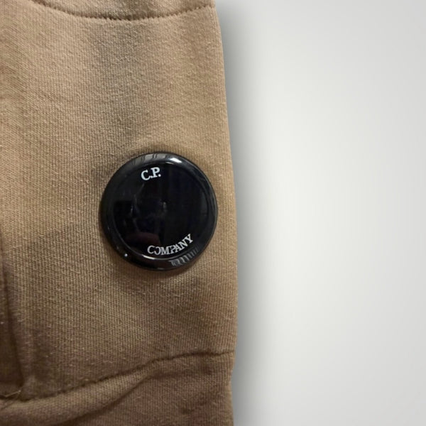 Détail de la lentille noire iconique C.P. Company sur la manche d'un sweat à capuche beige Secondstore en coton