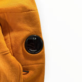Détail de la lentille noire emblématique sur la manche d'un sweat à capuche orange Secondstore en coton