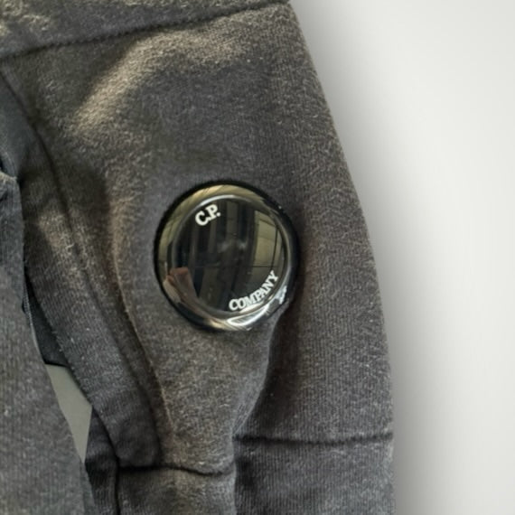 Détail de la manche noire d'un sweat-shirt Secondstore C.P. COMPANY avec la lentille signature sur poche zippée
