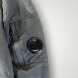 Détail de la manche d'un sweat-shirt gris Secondstore C.P. COMPANY avec poche zippée et lentille iconique noire