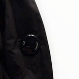 Détail de la manche d'une veste noire Secondstore C.P. Company avec l'emblématique lentille de protection